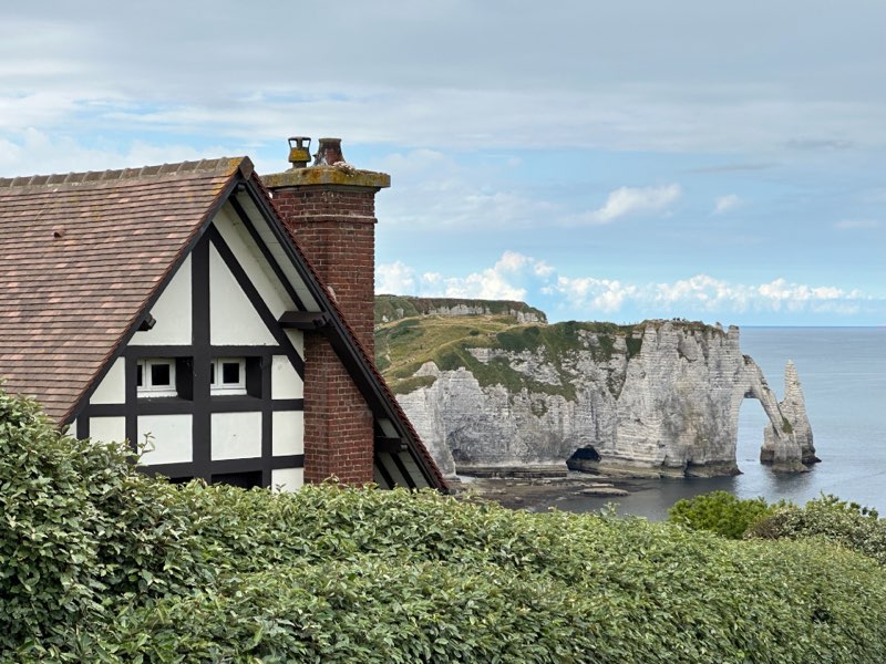 Half-timbered cottage with a chimney above green hedges near a coastal cliff