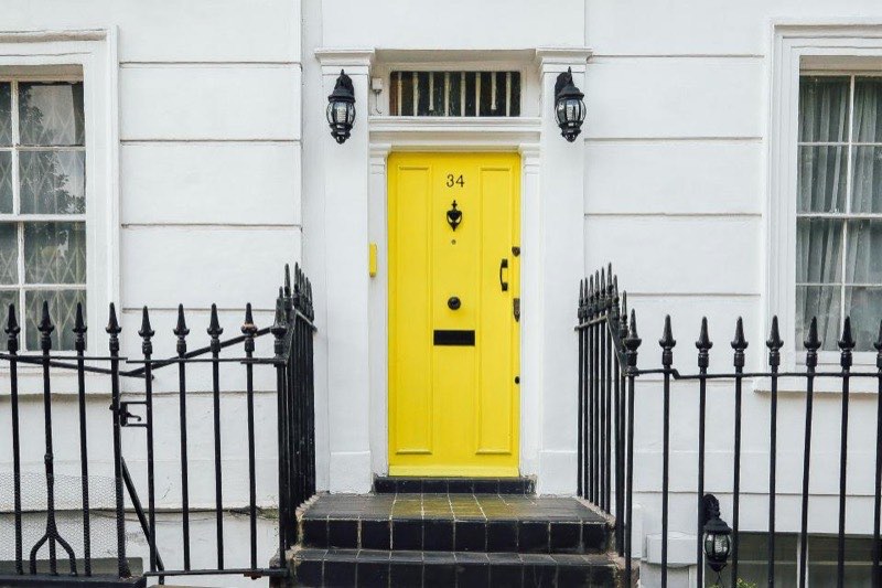 White townhouse facade with a yellow front door and iron railings